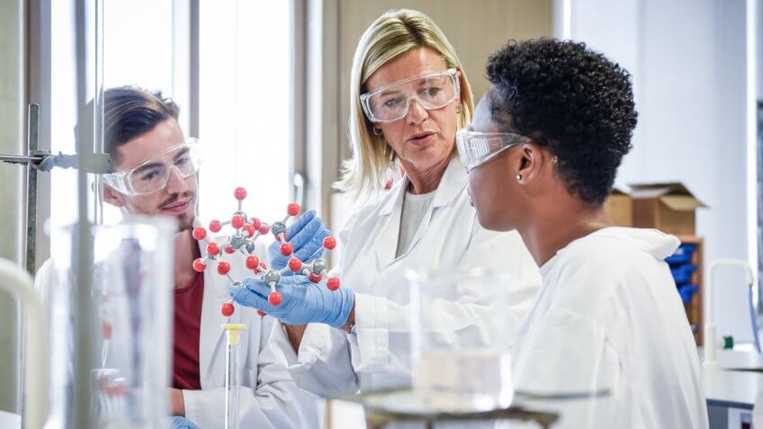 Two science students in laboratory wearing lab coats and safety goggles, learning about chemical structure.