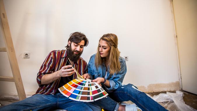 Hipster couple painting a house, sitting on the floor and choosing colors from a color swatch.