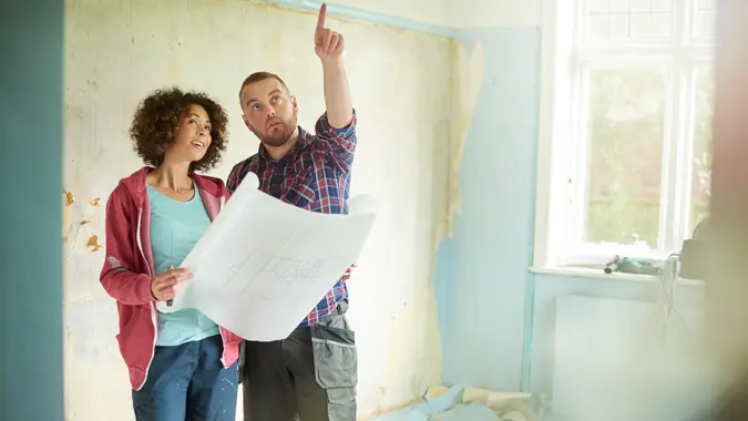 a young couple take time out from scraping walls in her new house to check against their architect plans.
