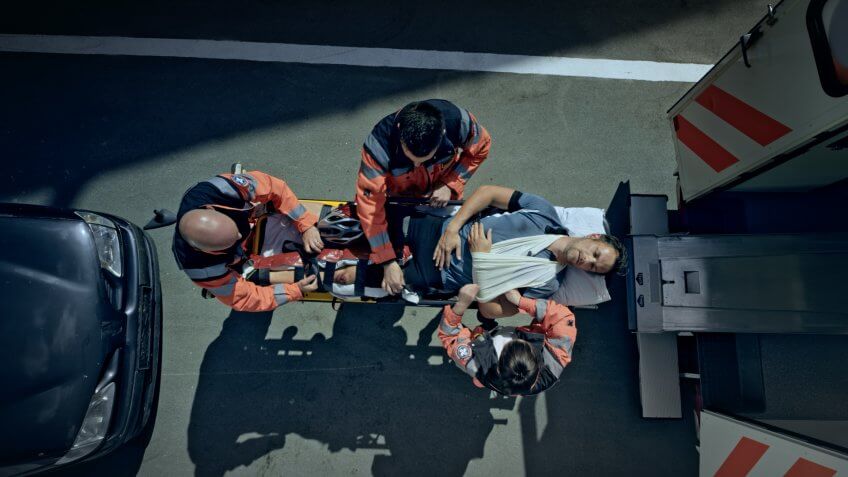 Male cyclist injured in car accident being loaded into ambulance.