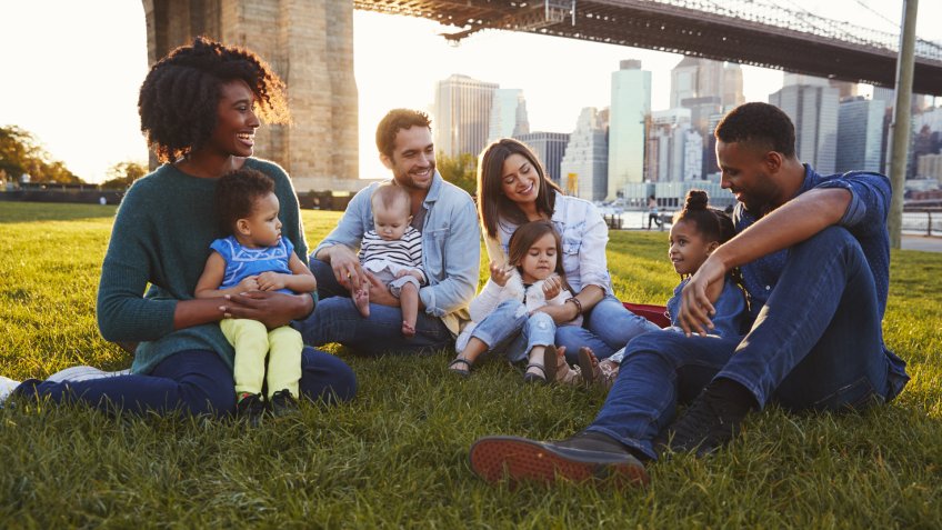 Two families with daughters sitting on lawn.