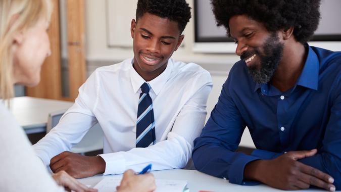 Father And Teenage Son Having Discussion With Female Teacher At High School Parents Evening.