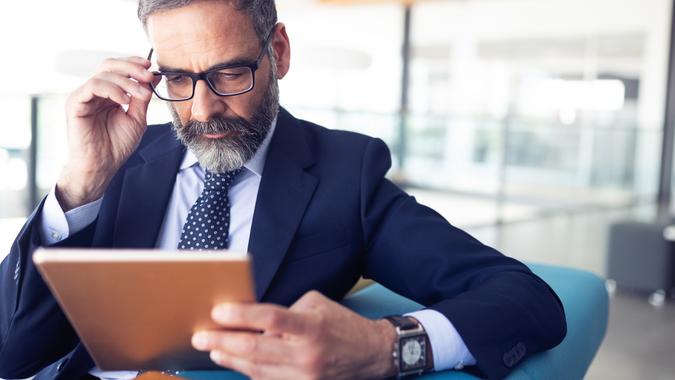 Serious man managing director of prosperous company is holding touch pad.