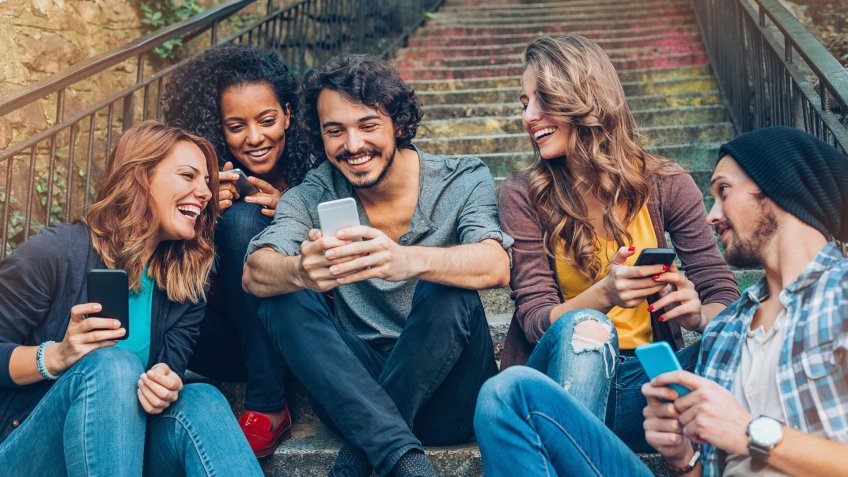 Multi-ethnic group of friends with smart phones sitting on a staircase.
