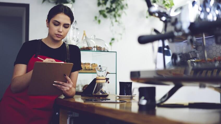 Concentrated professional administrative manager of coffee shop making revisions after working day using documentation and accounting of incomes from service and sale.