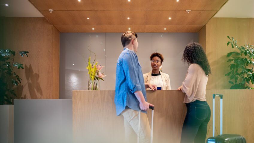 Mid adult couple talking to female receptionist.