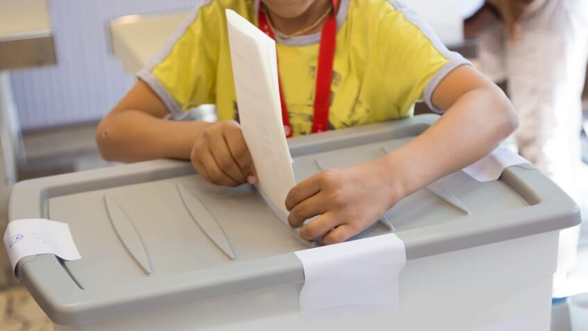 kid putting ballot in fake ballot box