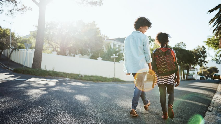 Rearview shot of a cheerful young mother and her daughter walking down the street together outside during the day.