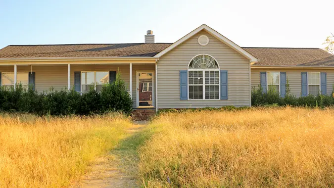 All too common scene of an unkempt, ranch style, home in the foreclosure process in a working class subdivision in the United States, with overgrown yard and bushes making it an eyesore to the neighborhood.