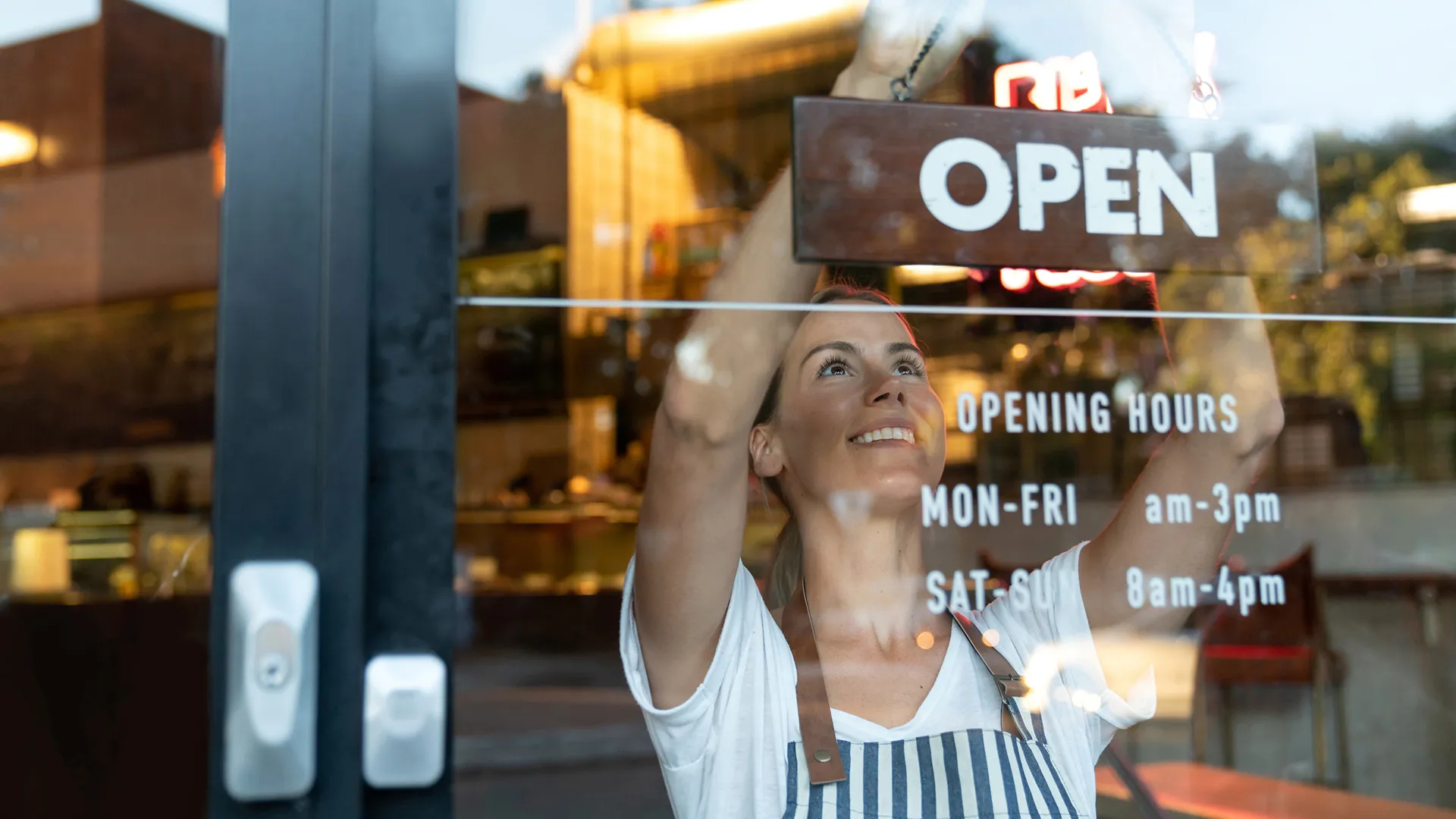Portrait of a happy business owner hanging an open sign on the door at a cafe and smiling - food and drinks concepts.