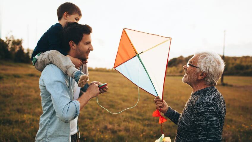 Photo of a three generations of men, who enjoy kite running and spending time together outdoors in the nature.