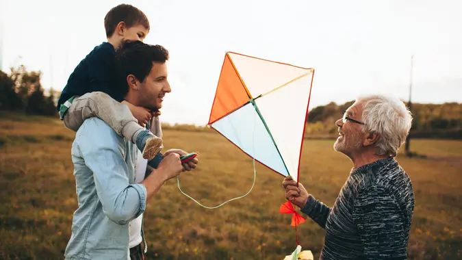 Photo of a three generations of men, who enjoy kite running and spending time together outdoors in the nature.
