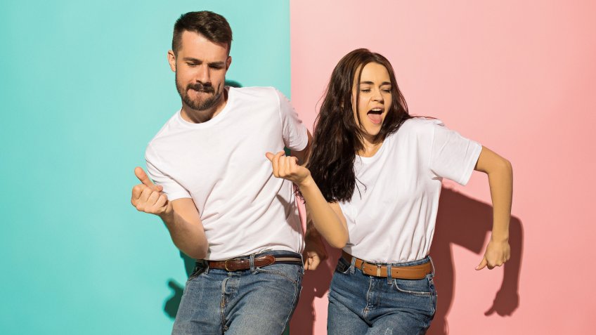A couple of young funny and happy man and woman dancing hip-hop at studio on blue and pink trendy color background.