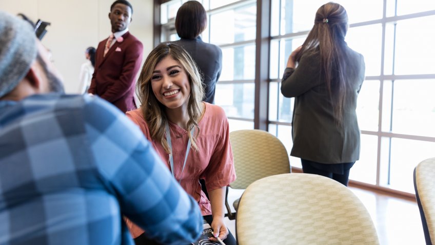 Smiling young woman shakes hands with an associate while attending a conference or seminar.