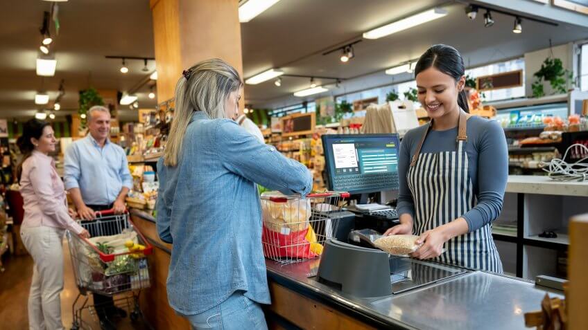 Cheerful employees at supermarket doing checkout for customers **DESIGN ON SCREEN WAS MADE FROM SCRATCH BY US**.