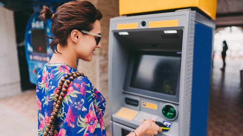 Tourist on vacation withdrawing money on ATM with smartphone.