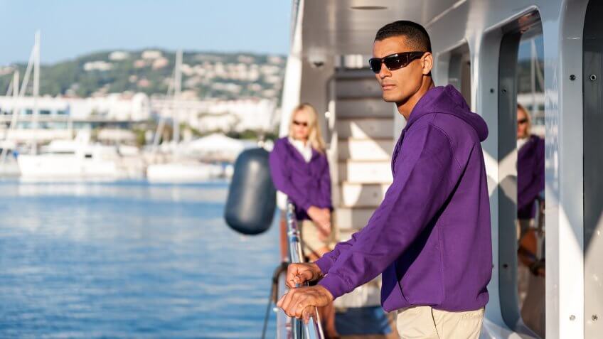 Horizontal color image of crew members standing on luxury yacht boat at harbor during sunny day.