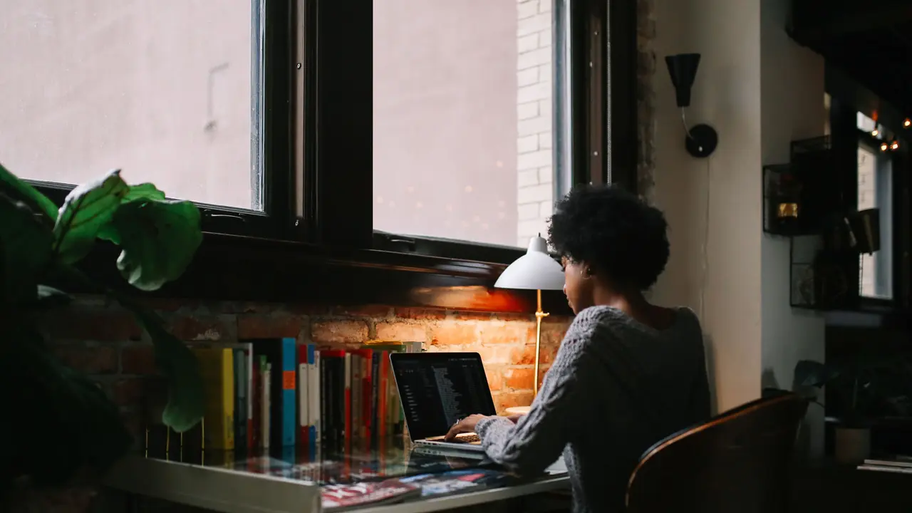 Young mixed race woman sitting at the desk in her apartment in downtown Los Angeles, typing at the laptop, finishing up her freelancer work or studies while having a coffee.