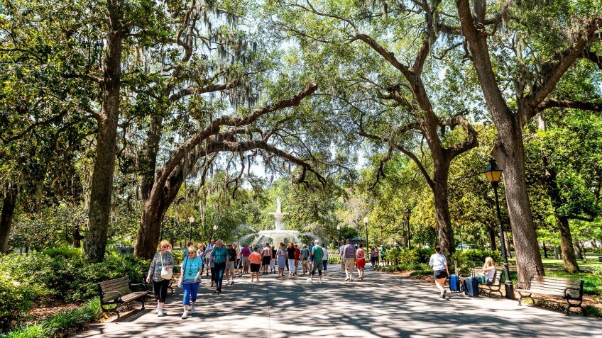 Savannah, USA - May 11, 2018: Famous water fountain in Forsyth park, Georgia during sunny day in summer with people walking on alley street.