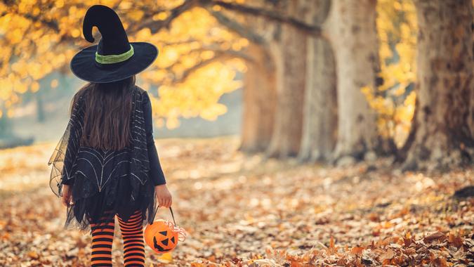 Little girl in witch costume having fun outdoors on Halloween trick or treat.