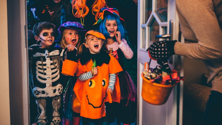 Group of children and their parents playing trick or treat on Halloween.