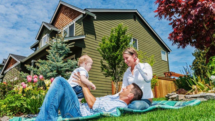 Photo of a happy family in front of their home, enjoying a sunny day in the yard on a blanket.