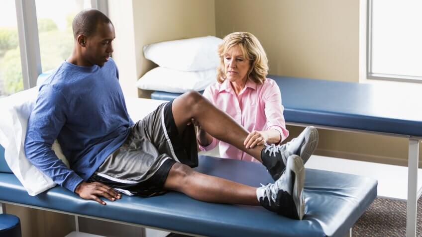 A female physical therapist examining a young African American man on a treatment table.