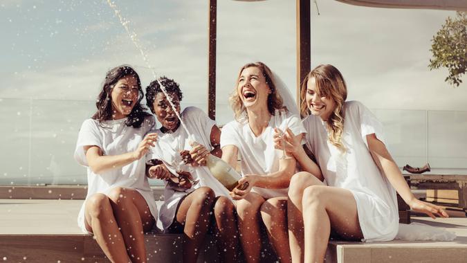 Cheerful bride and bridesmaids celebrating hen party with champagne while sitting on rooftop.