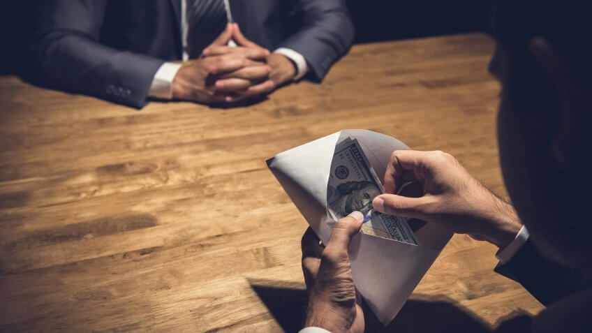 Businessman checking money, US dollars, in the envelope just given by his partner - bribery and corruption concepts.