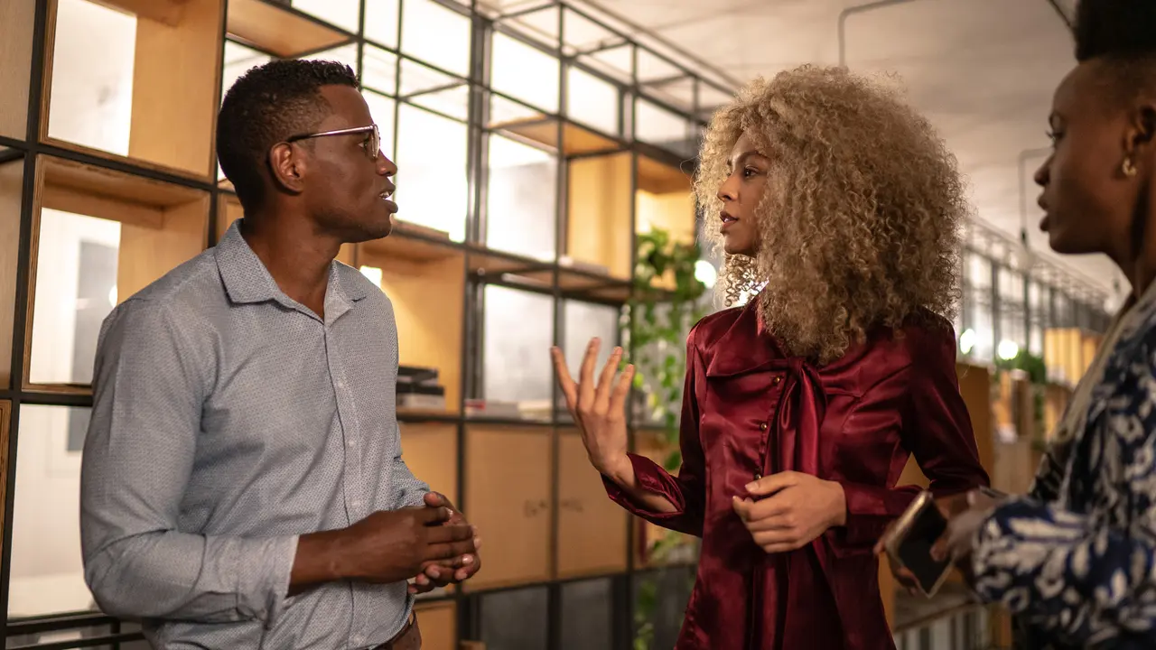 Three business people dressed in a professional way having a discussion while walking in the well-lit office.