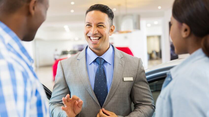 handsome vehicle dealer talking to customers in showroom.