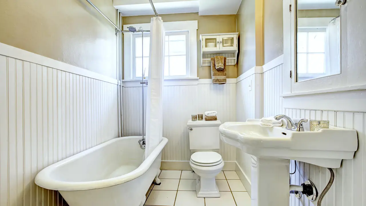 Claw foot tub in bright bathroom with white wall trim, washbasin stand and toilet.