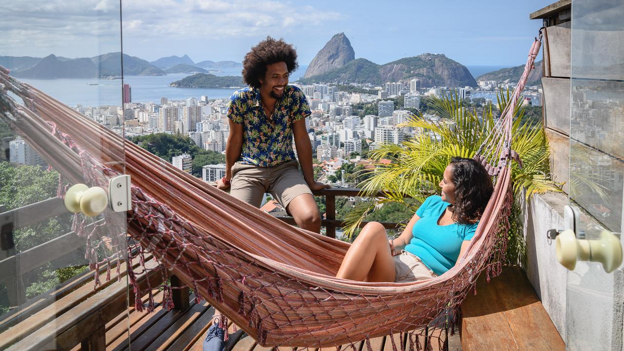 Brazilian couple smiling at each other on decking, woman in hammock, Sugar Loaf Mountain in the distance.