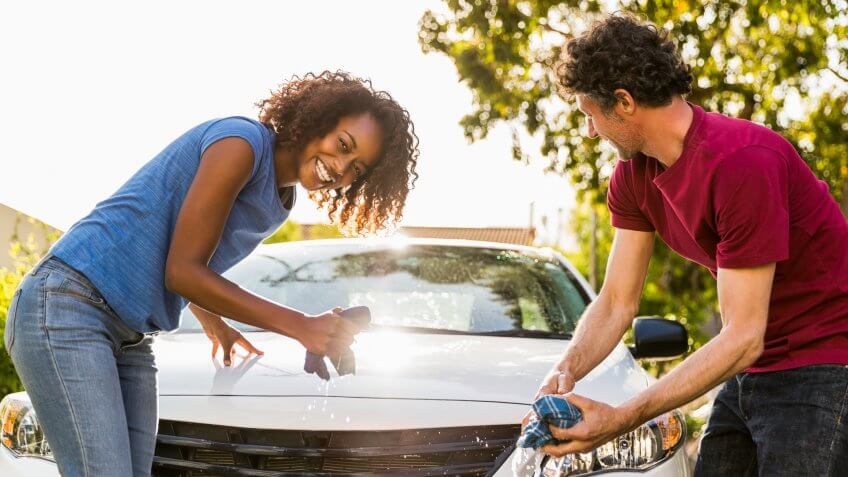 Portrait of cheerful woman cleaning car with man at yard.