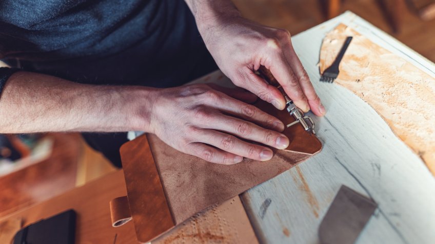 Close-up image of craftsperson creasing the edges of leather piece.