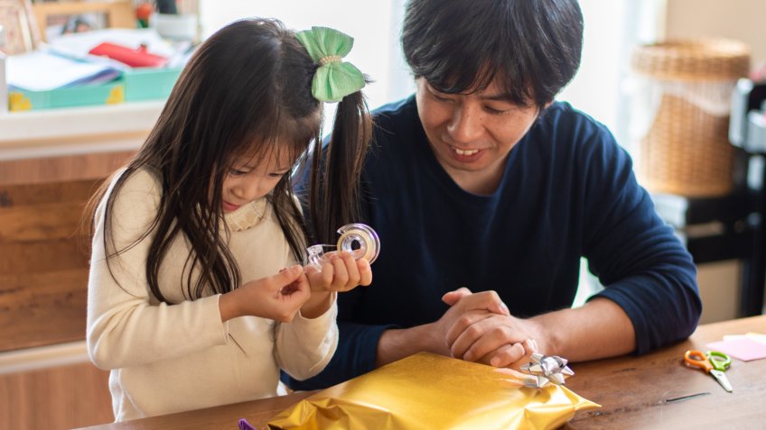 A candid front view photo of a Japanese father wrapping Christmas presents with his daughter.