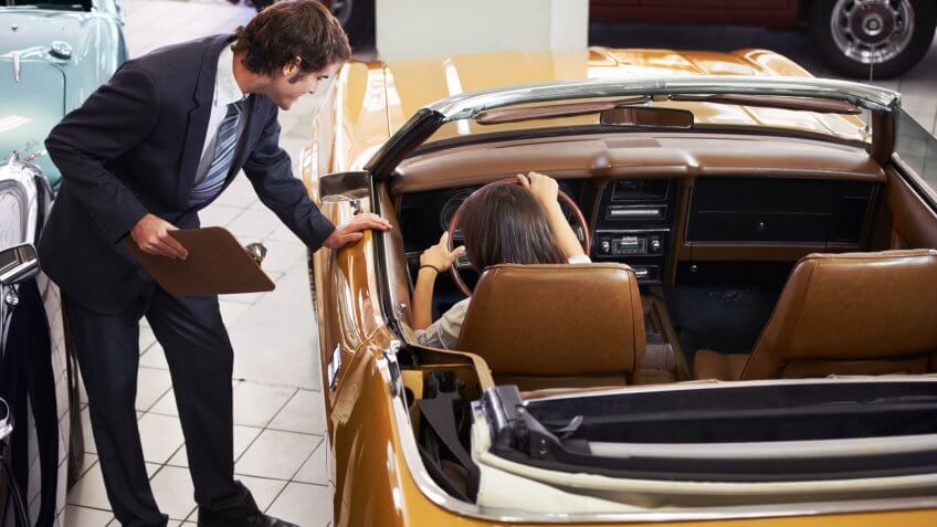 Handsome young classic car salesman standing in the dealership and helping a client make a decision.