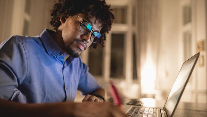 Young and determined black student studying at night at home, with a help of a laptop computer.