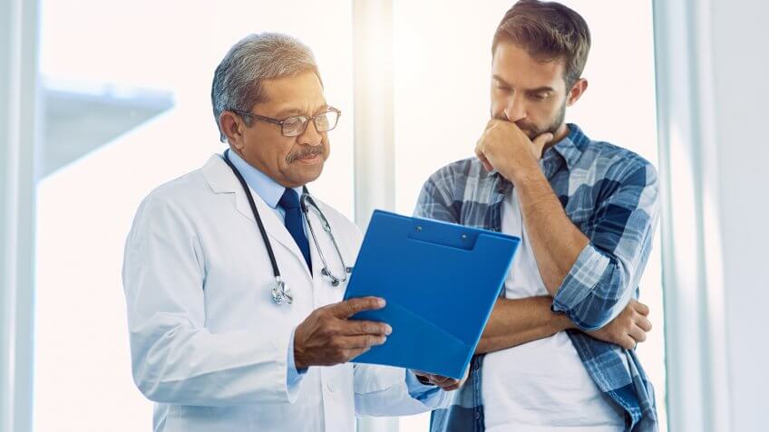 Shot of a confident mature male doctor showing test results to a patient inside of a hospital during the day.