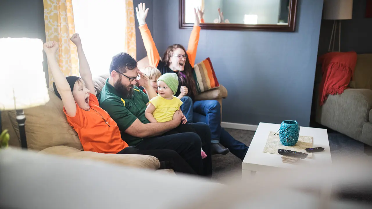 A happy family with three children have fun goofing off while watching a sports game on the television.