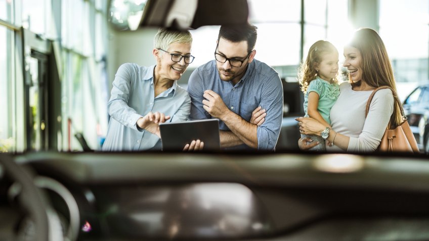Happy family and car salesperson using touchpad in a showroom.