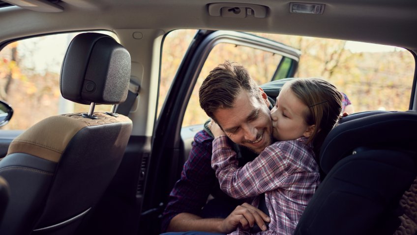Close up of a father helping his daughter strap her seatbelt.
