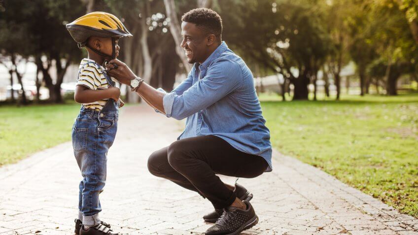 African man putting helmet on cute boy at the park.