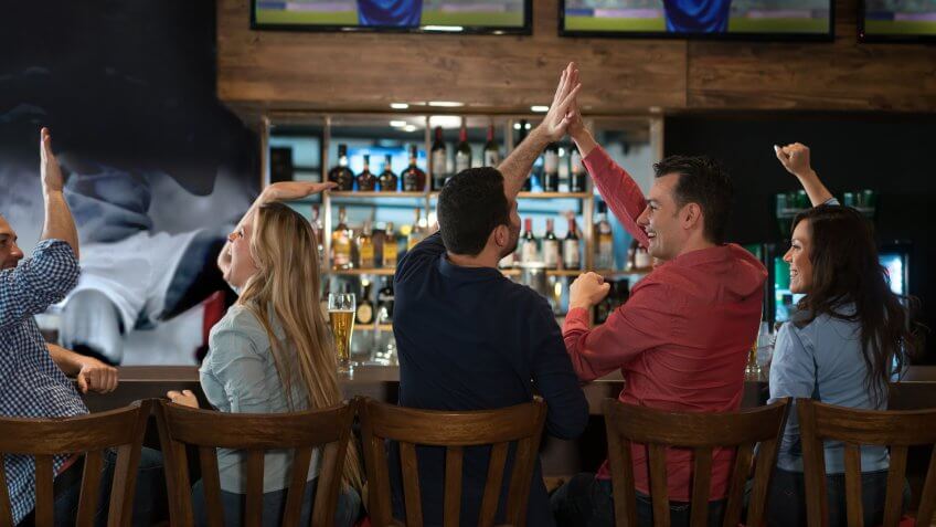 Happy group of friends watching sports at the bar and drinking beer.
