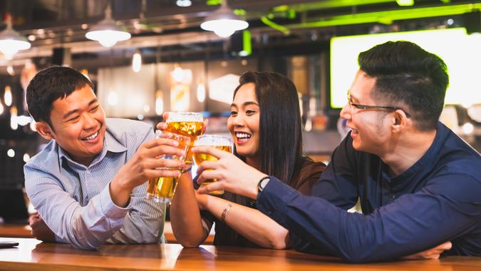 Group of happy Asian friend or office colleague coworker celebrate toast beer pint together at pub restaurant or night club.