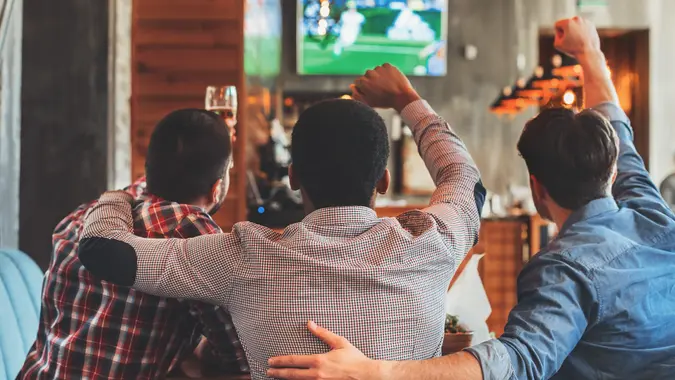Three men watching football on TV in sport bar, back view.