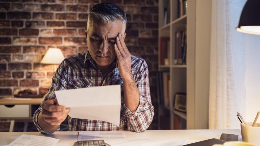 Worried mature man checking his domestic bills at home, he is concerned and reading his financial statements.