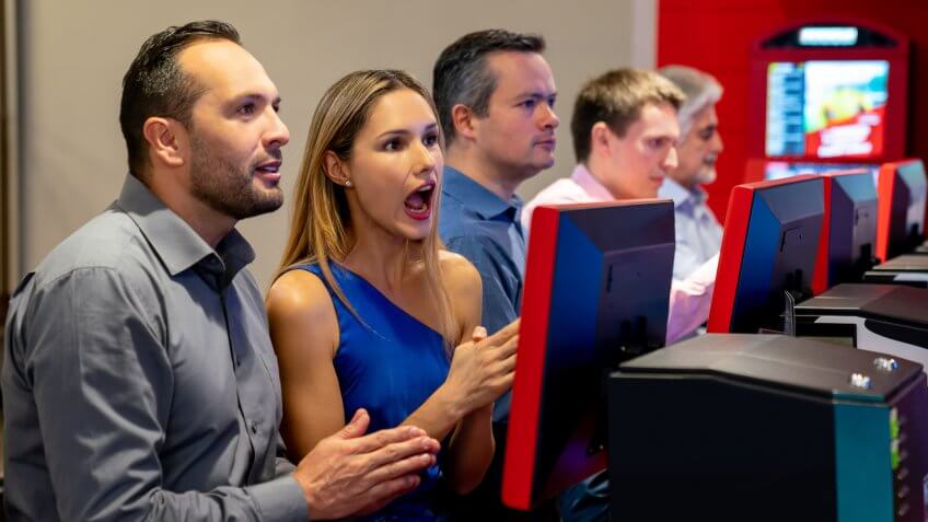 Escited and prayful couple hoping to win a bet at the casino and other customers betting at the background.
