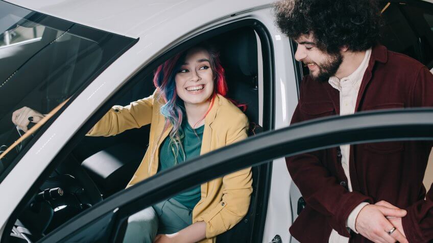 overhead view of cheerful girl with colored hair sitting in car and looking at curly man.