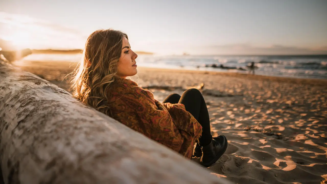 Young woman sitting by a beach at sunset in winter.